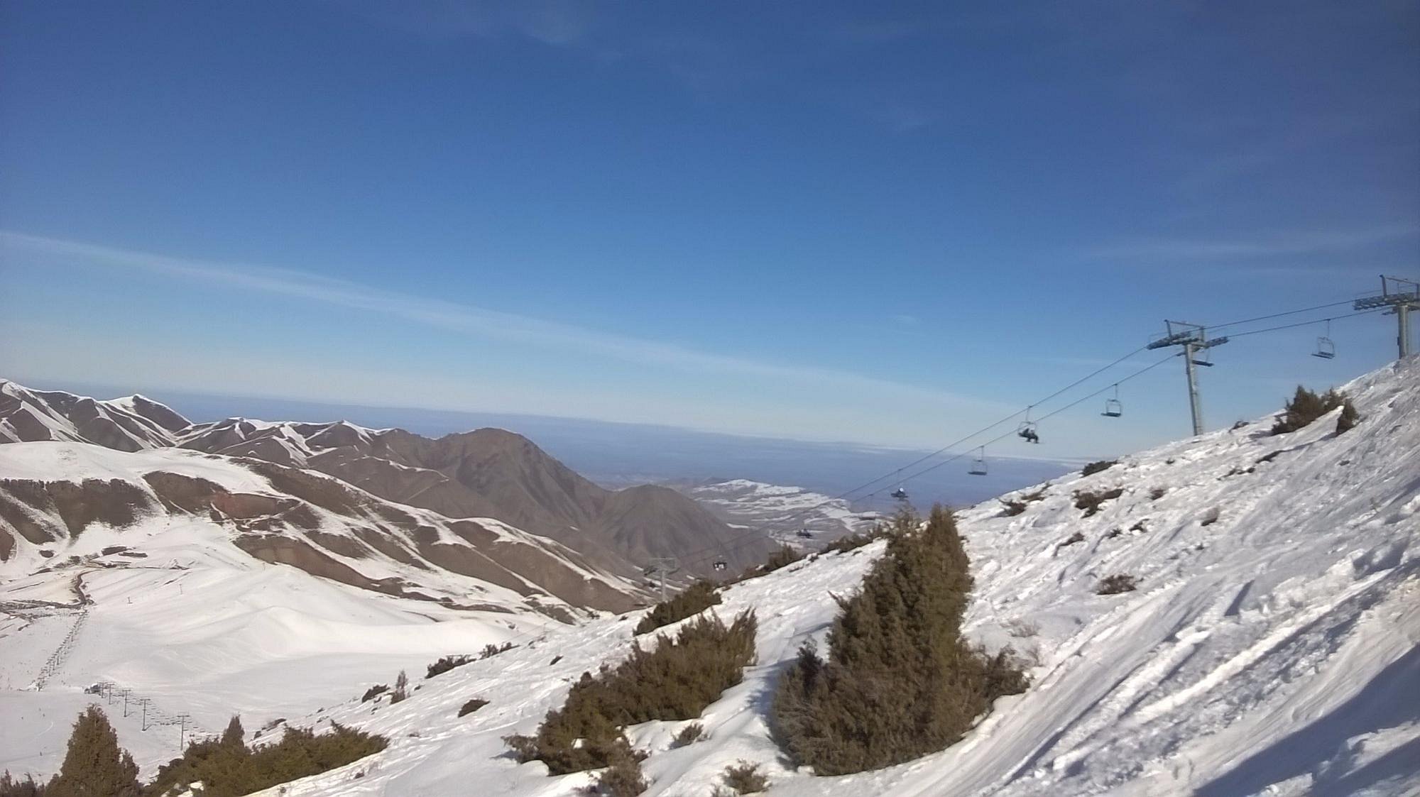 A skier enjoying a winter day in Chunkurchak, Kyrgyzstan, with a ski lift and chalet in the backdrop of the popular ski resort.