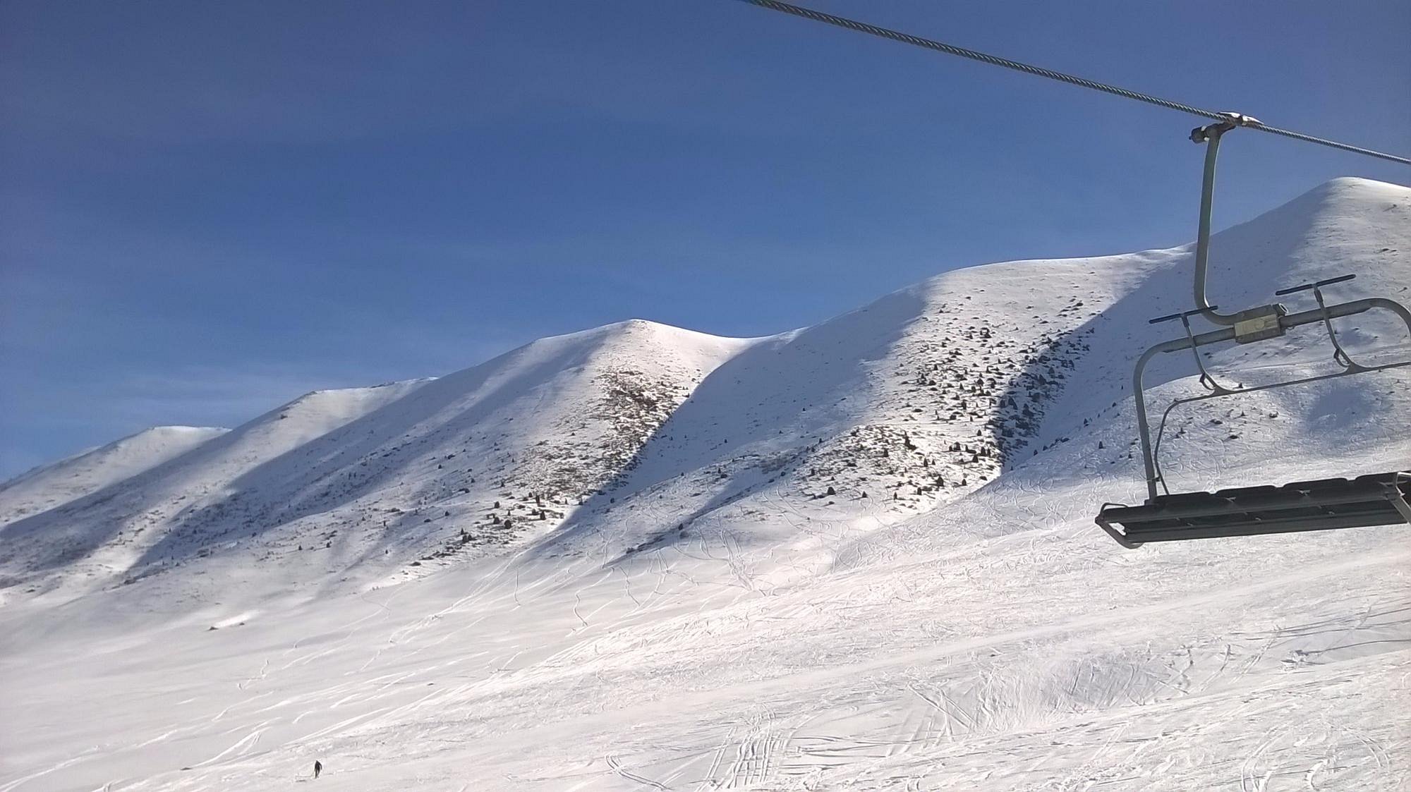 A skier enjoying the snowy slopes in Chunkurchak, Kyrgyzstan. Glimpse of a ski lift, chalet, and resort in the wintry landscape.