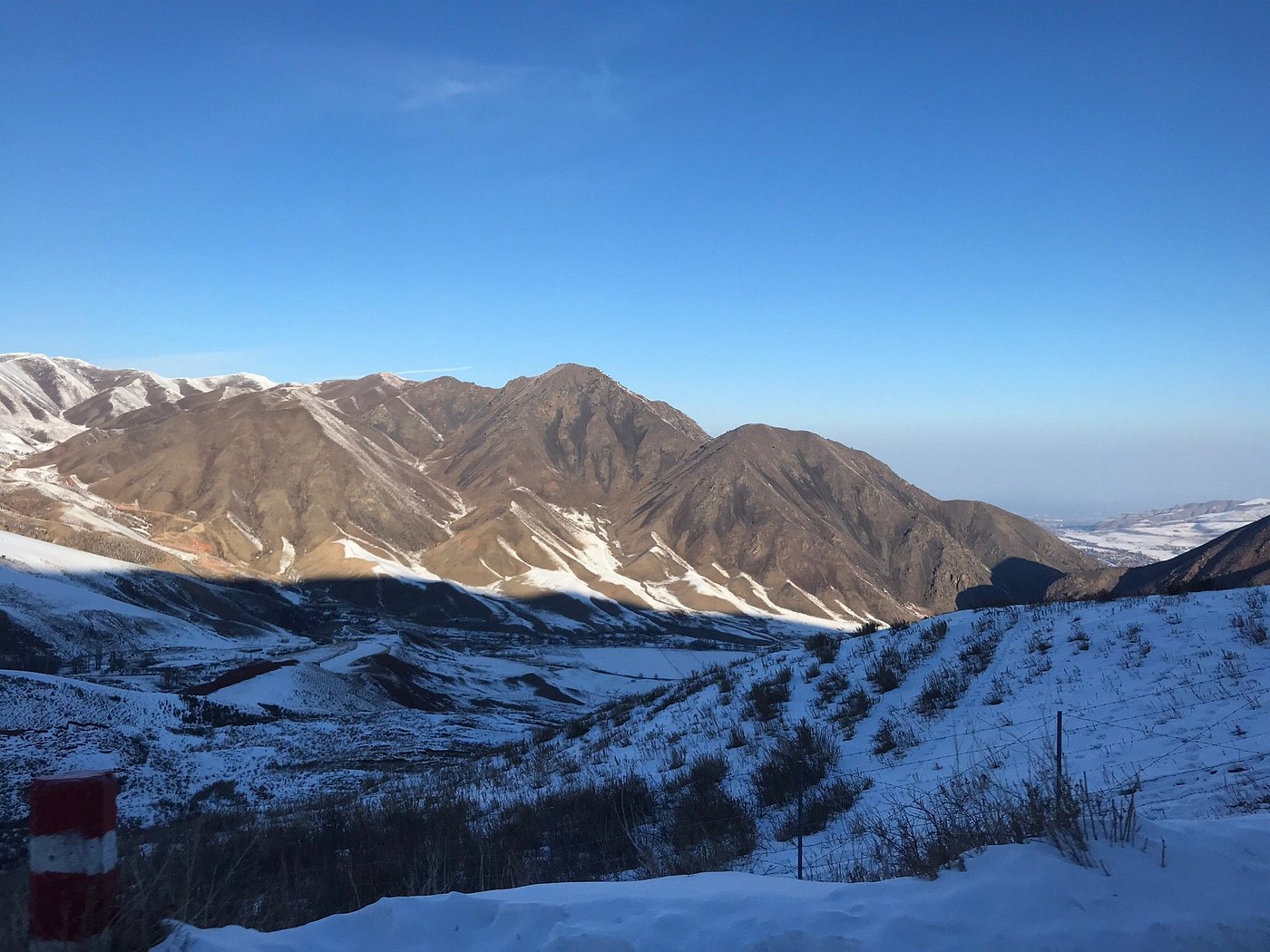 Stunning winter vista in Chunkurchak, Kyrgyzstan showcasing a frosted mountain landscape and whitened trees. A winter sports scene is visible in the distance alongside a cozy chalet, invoking a serene, chill atmosphere.