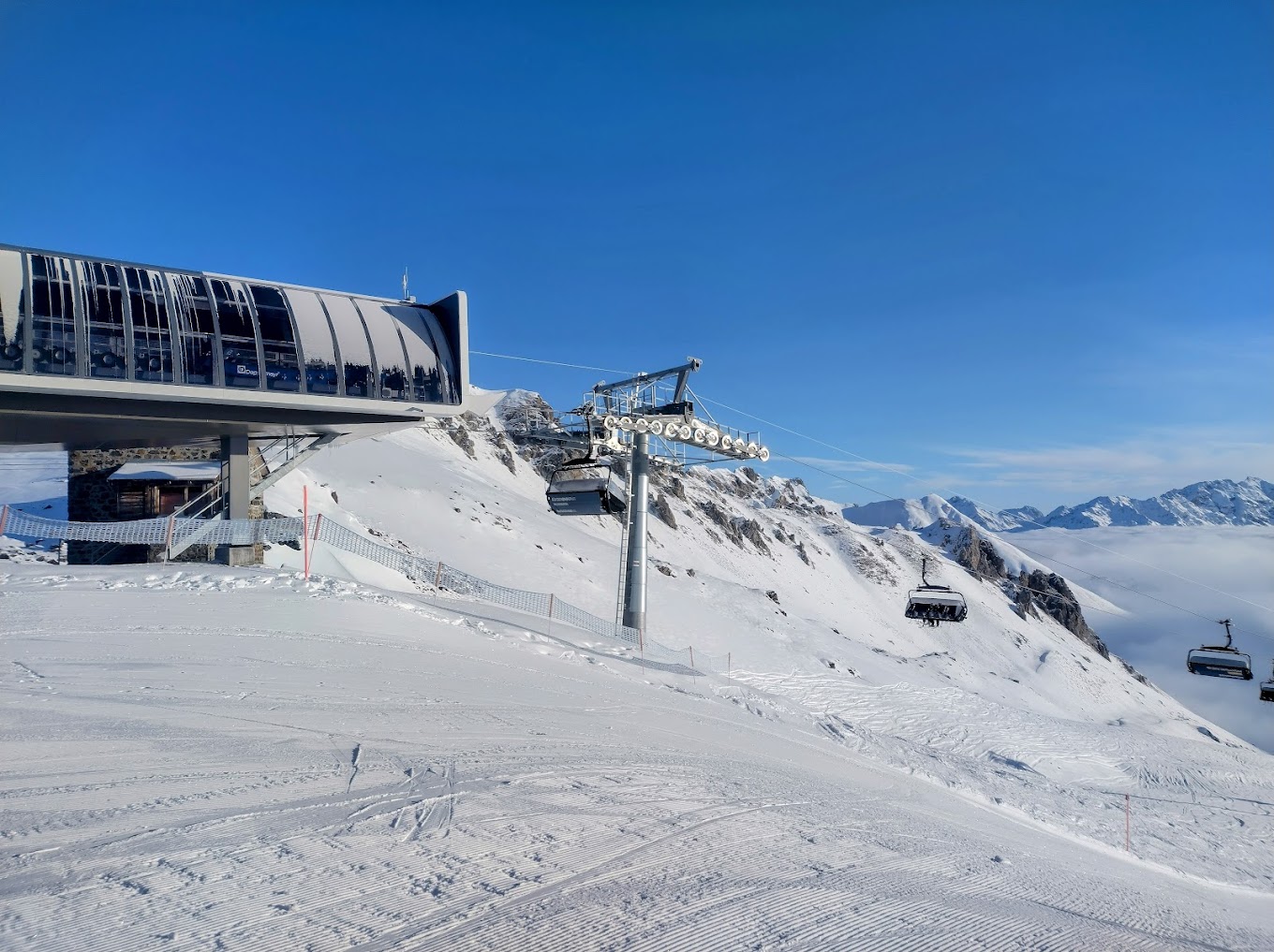 A scenic view from Parsenn ski resort in Davos Eastern Switzerland featuring a ski lift that travels above the winter sports centre. Challets peek out from the snowy landscape amidst a vibrant winter sports scene.