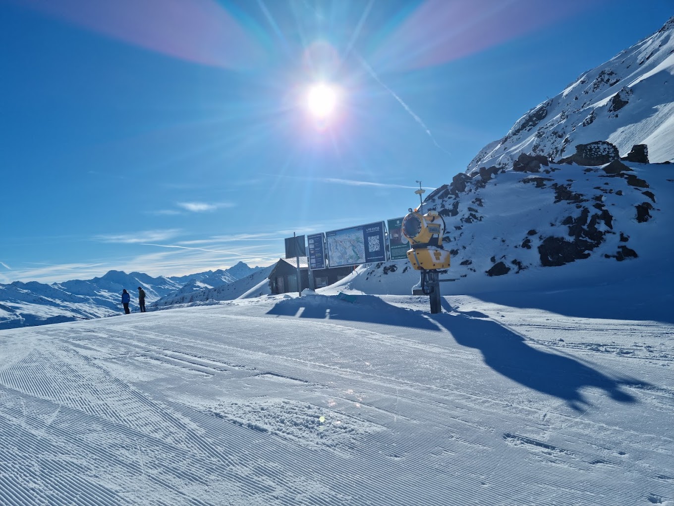 Winter scene at Parsenn ski resort in Davos, Switzerland featuring skiers, a chalet, and a bustling winter sports center enclosed by snowy landscape.