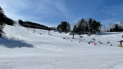 Winter sports scene at Swain Resort in New York, featuring a skier descending a snowy slope, a chalet in the background, and hints of further winter sports facilities.