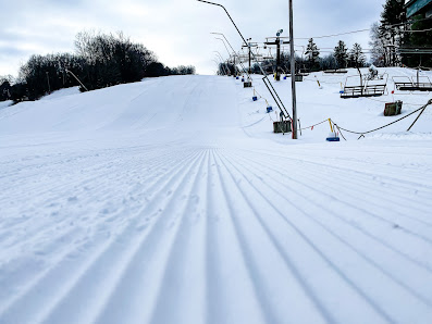 A skier glides down the slopes at Swain in Chautauqua-Allegheny, New York. The cozy chalet of the ski resort is visible in the background of this active winter sports scene.