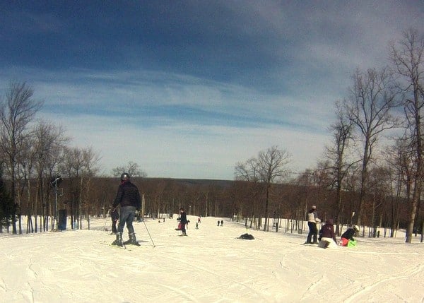 A beautiful winter sports scene at Jack Frost Mountain Pennsylvania with a skier making their way down the snowy slopes. The landscape is dotted with the ski resort buildings and ski lifts.