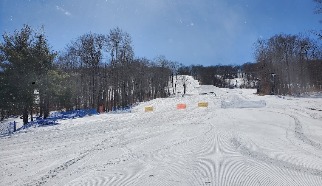 Winter sports scene at Jack Frost Mountain in Pennsylvania, featuring a bustling ski resort. Skiers are seen descending snow-covered slopes, while others are carried upwards by a ski lift.