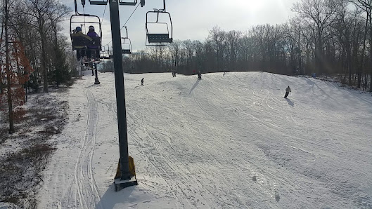 A vibrant winter sports scene at Jack Frost Mountain in Pennsylvania featuring a ski lift transporting skiers uphill. The ski resort bustles with activity as a skier prepares for a slope creating a lively atmosphere at this winter sports center.