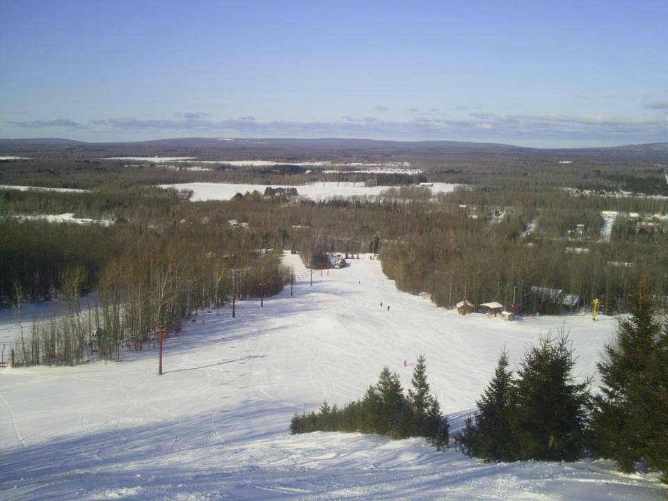 Winter sports enthusiasts enjoying a day at Big Powderhorn Mountain, a popular ski resort in Michigan. Visible is a ski lift ascending the snow-covered mountain with a skier and a chalet included in the scene.