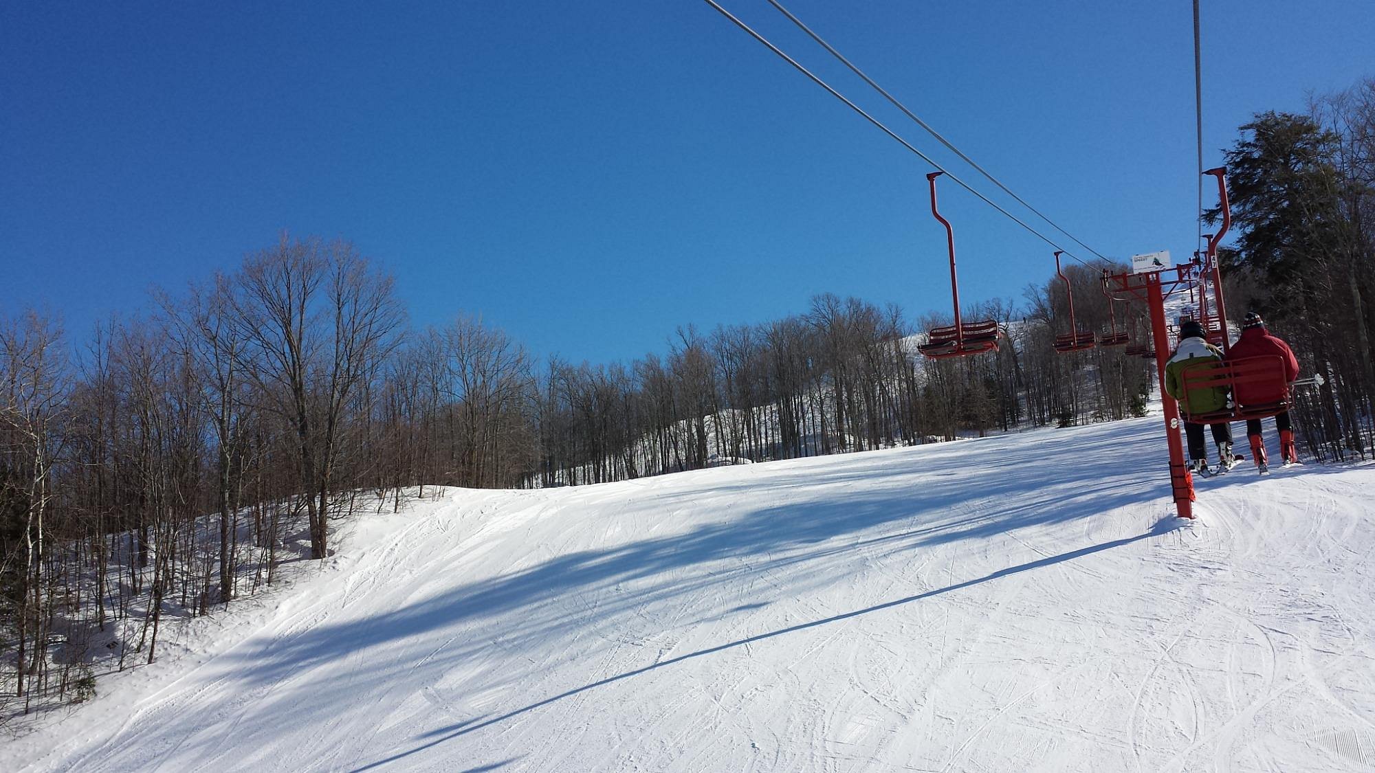 Winter sports enthusiasts enjoy a day at Big Powderhorn Mountain ski resort in Bessemer, Michigan. Skiers ascend the mountain on a ski lift, with a charming chalet nestled amidst the snowy landscape.