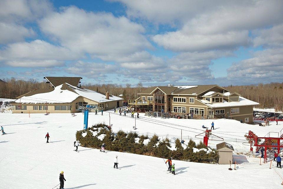 A winter sports scene at Big Powderhorn Mountain ski resort in Bessemer Michigan. Various enthusiasts enjoy the snowy slopes with a ski lift visible in the distance. The scene encapsulates the beauty of winter sports.
