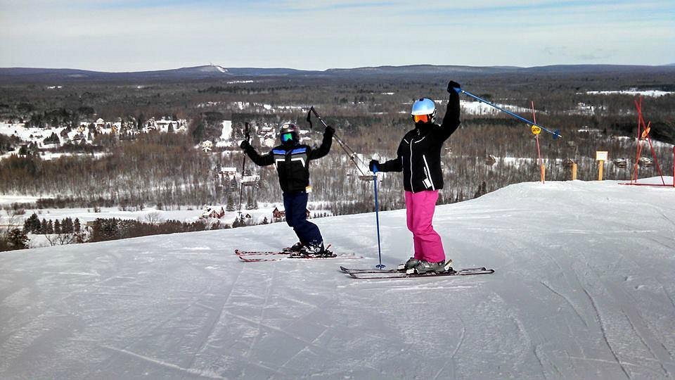 A skier enjoying a winter sports scene at Big Powderhorn Mountain a ski resort in Bessemer Michigan. The scenic backdrop includes a ski lift and a family skiing in the distant slope.
