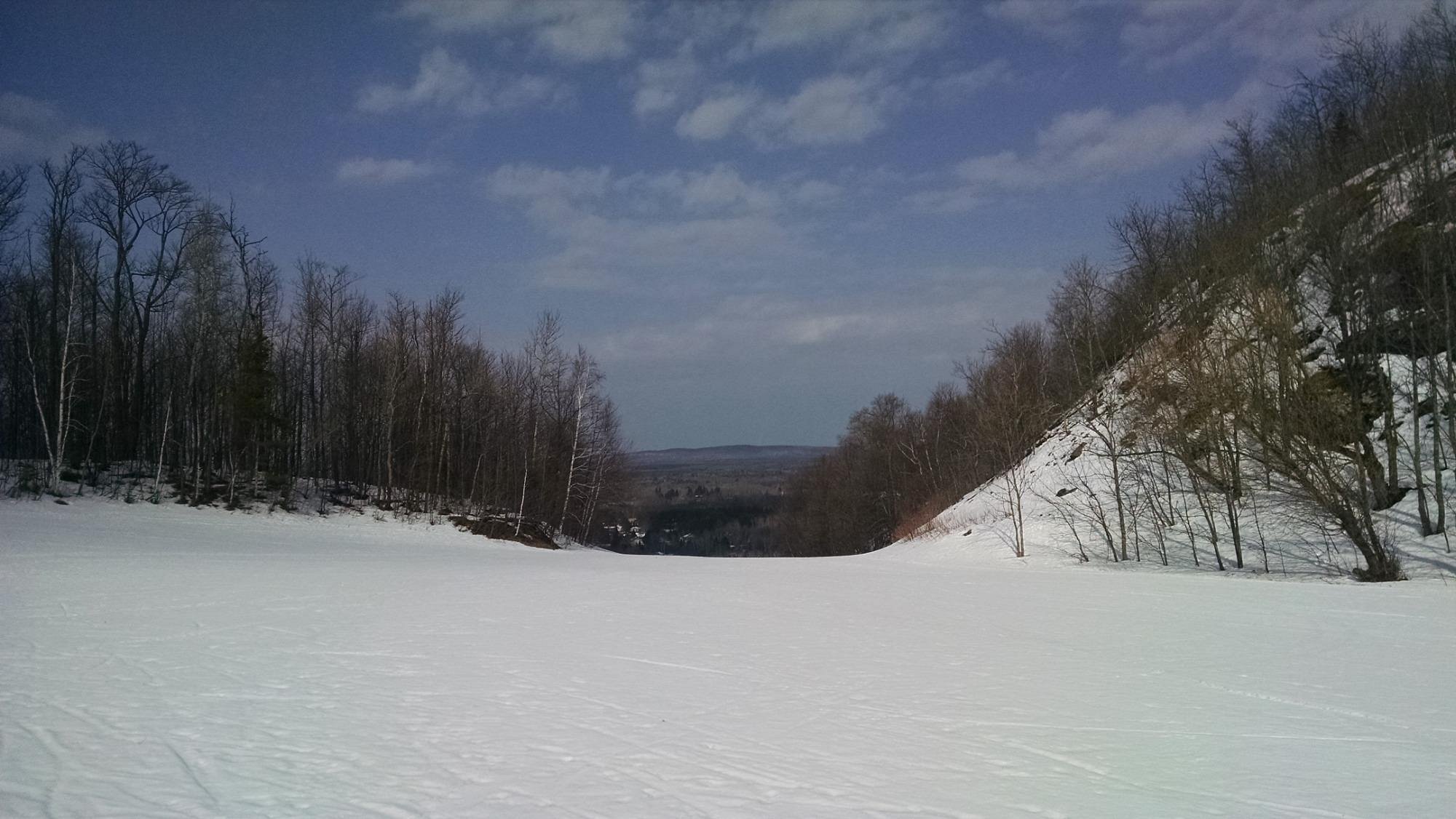 A tranquil winter scene at Big Powderhorn Mountain in Bessemer Michigan with skiers enjoying the slopes. A charming challet nestles nearby surrounded by the idyllic snowy mountain landscape of the ski resort.