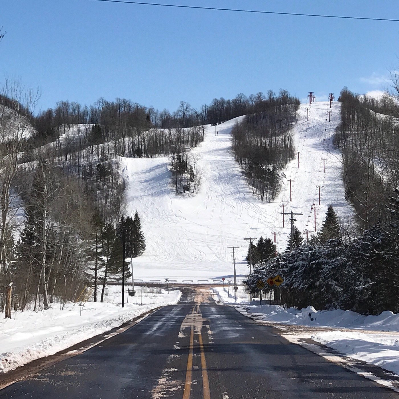 A winter sports scene at Big Powderhorn Mountain ski resort in Bessemer Michigan featuring snow-covered slopes a mountain backdrop and a ski lift.