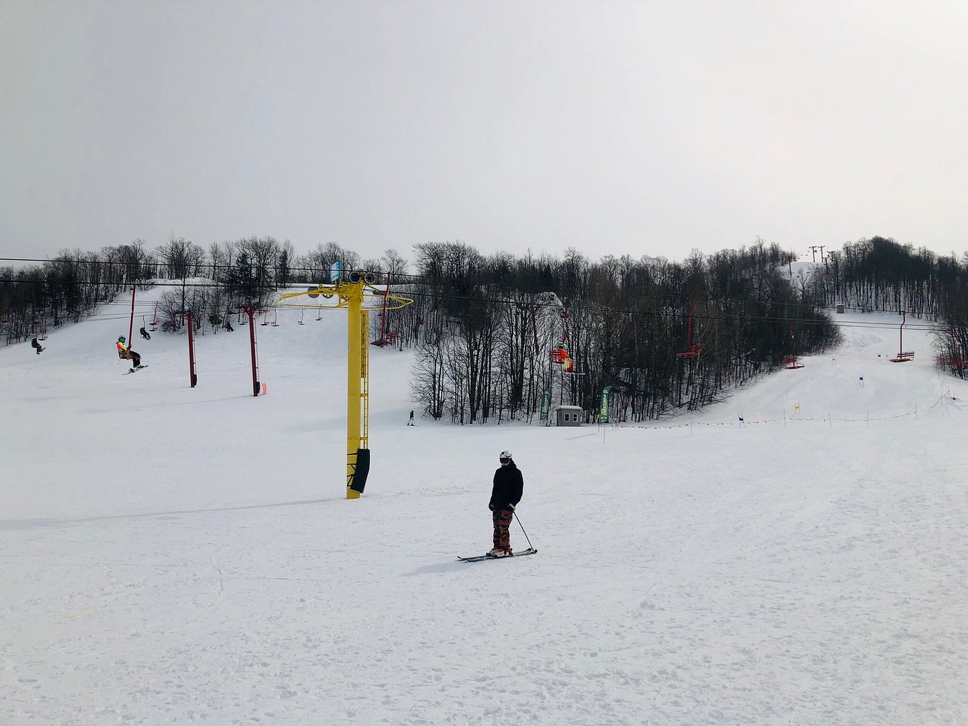 A skier and a snowboarder engaging in winter sports at Big Powderhorn Mountain ski resort in Bessemer Michigan with a ski lift visible in the background.