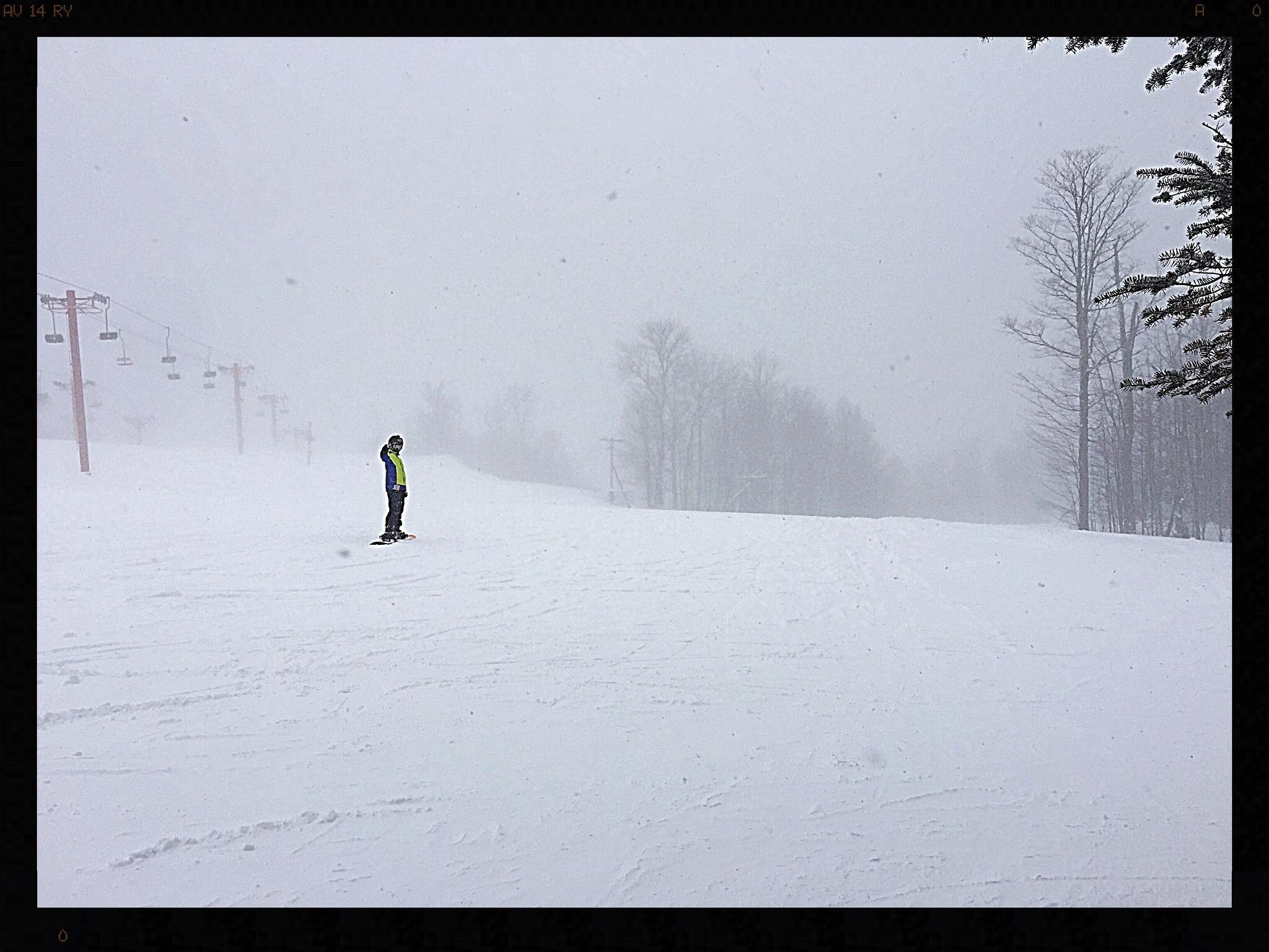 A skier gliding down Big Powderhorn Mountain in Michigan, with a ski lift and chalet subtly visible in the wintry scene.