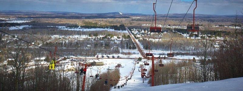 Ski lift ascending Big Powderhorn Mountain at a ski resort in Bessemer, Michigan, USA, amidst a lively winter sports scene with a chalet in the backdrop.