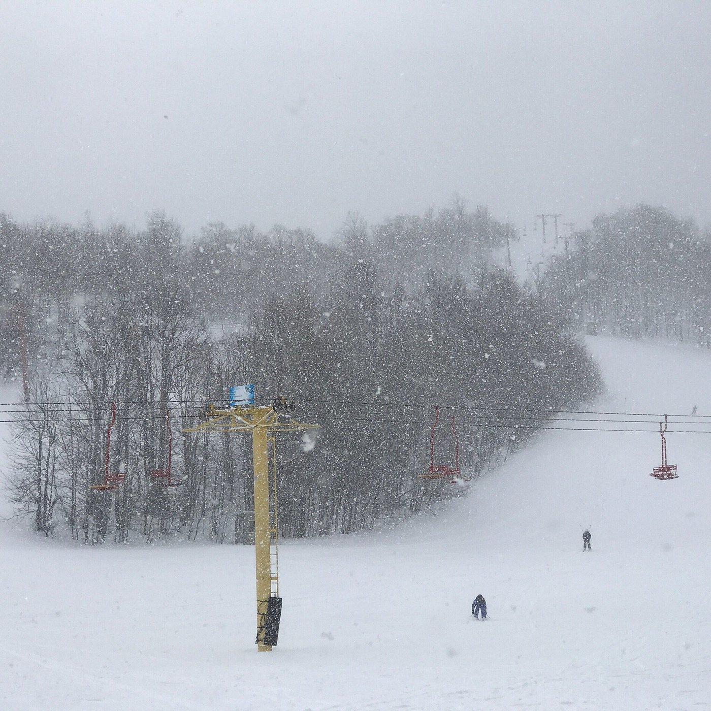 A lively winter sports scene at Big Powderhorn Mountain in Bessemer, Michigan, featuring a bustling ski resort with a ski lift amidst a beautiful snowy landscape.