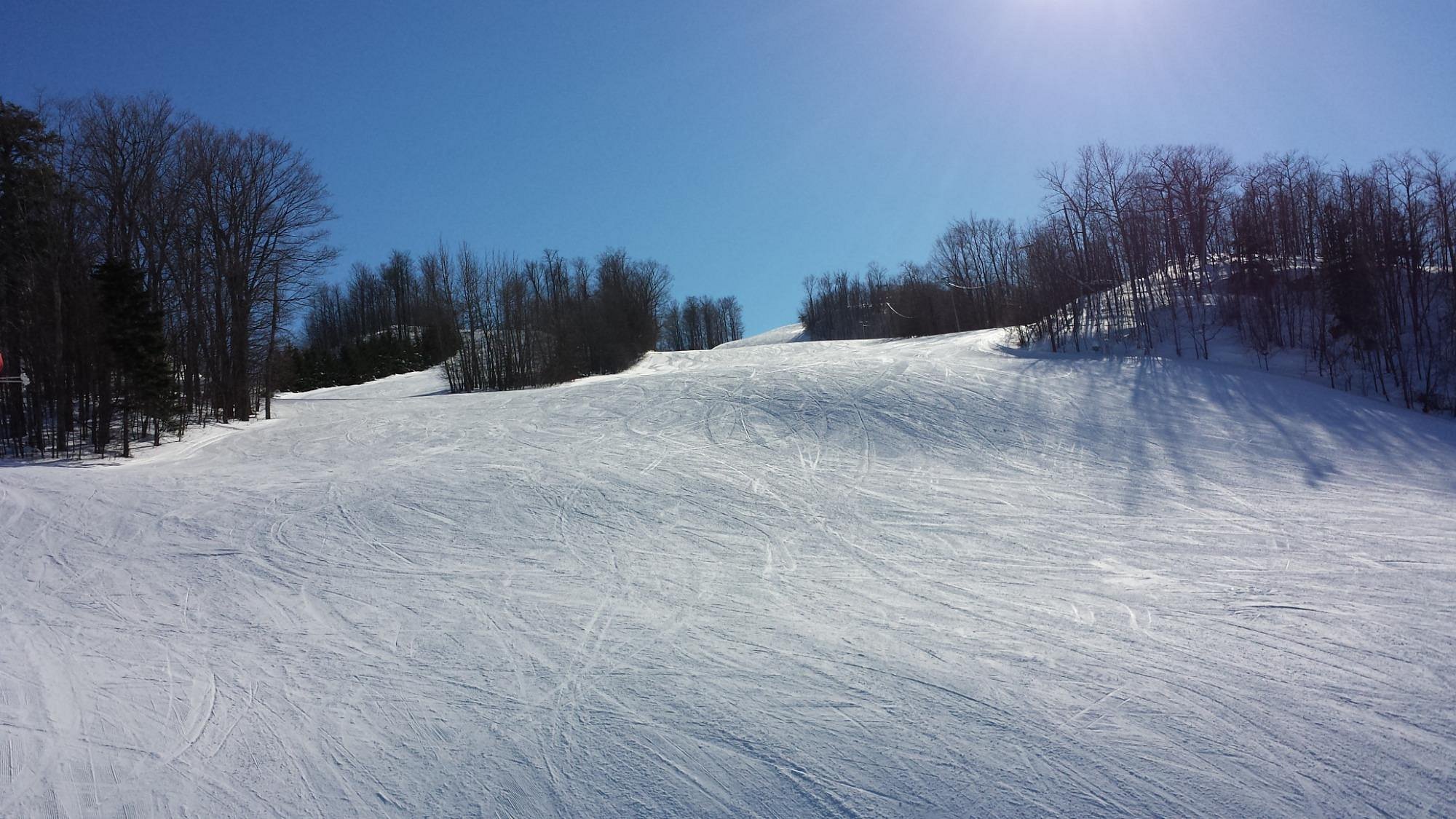 A lively winter scene at Big Powderhorn Mountain in Bessemer Michigan showcasing a skier enjoying the snow-covered slopes with a charming chalet and vast ski resort in the background.