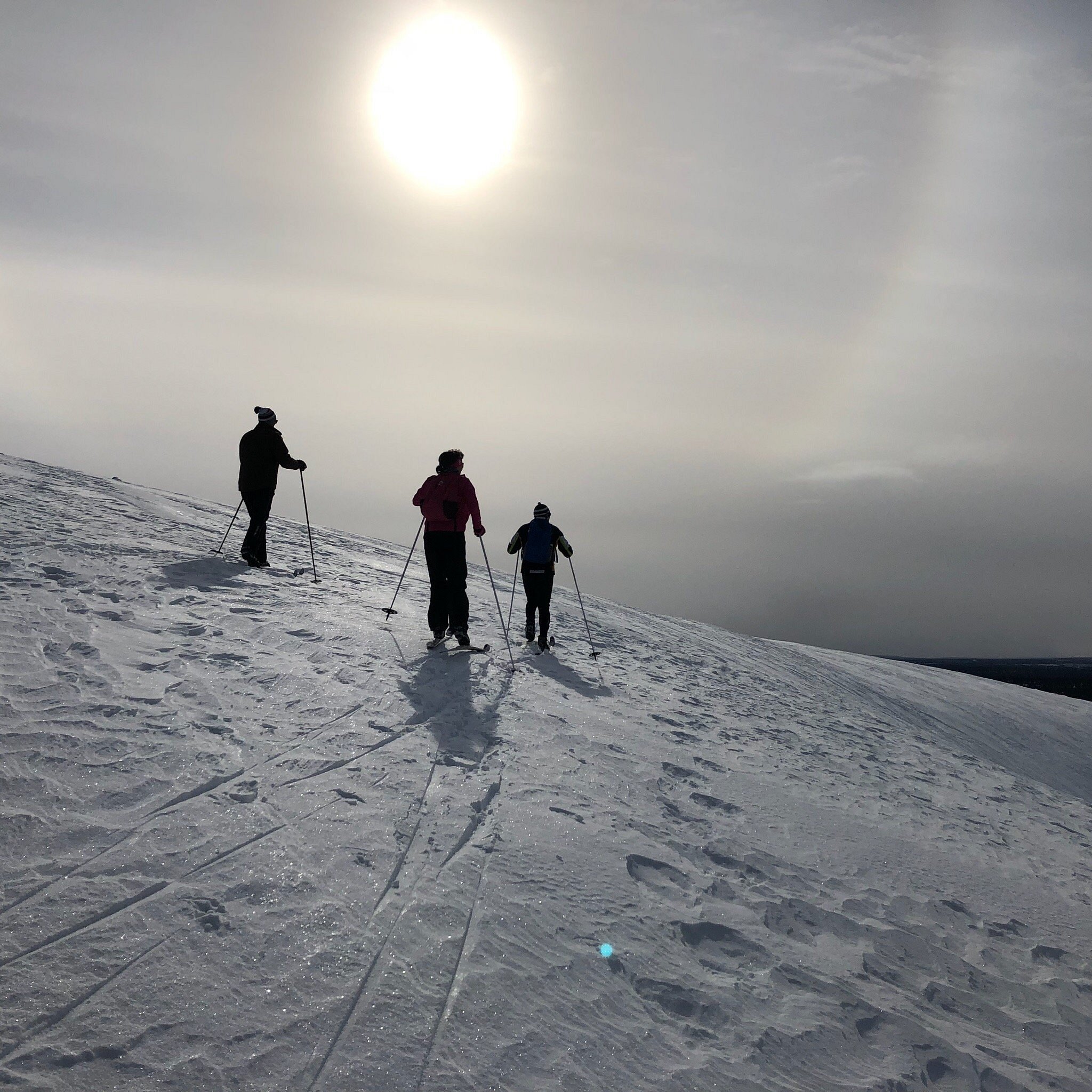 A winter sports scene in Saariselkä, Lapland, with a group of people, possibly a family, skiing down a slope. A chalet can be seen in the distance.