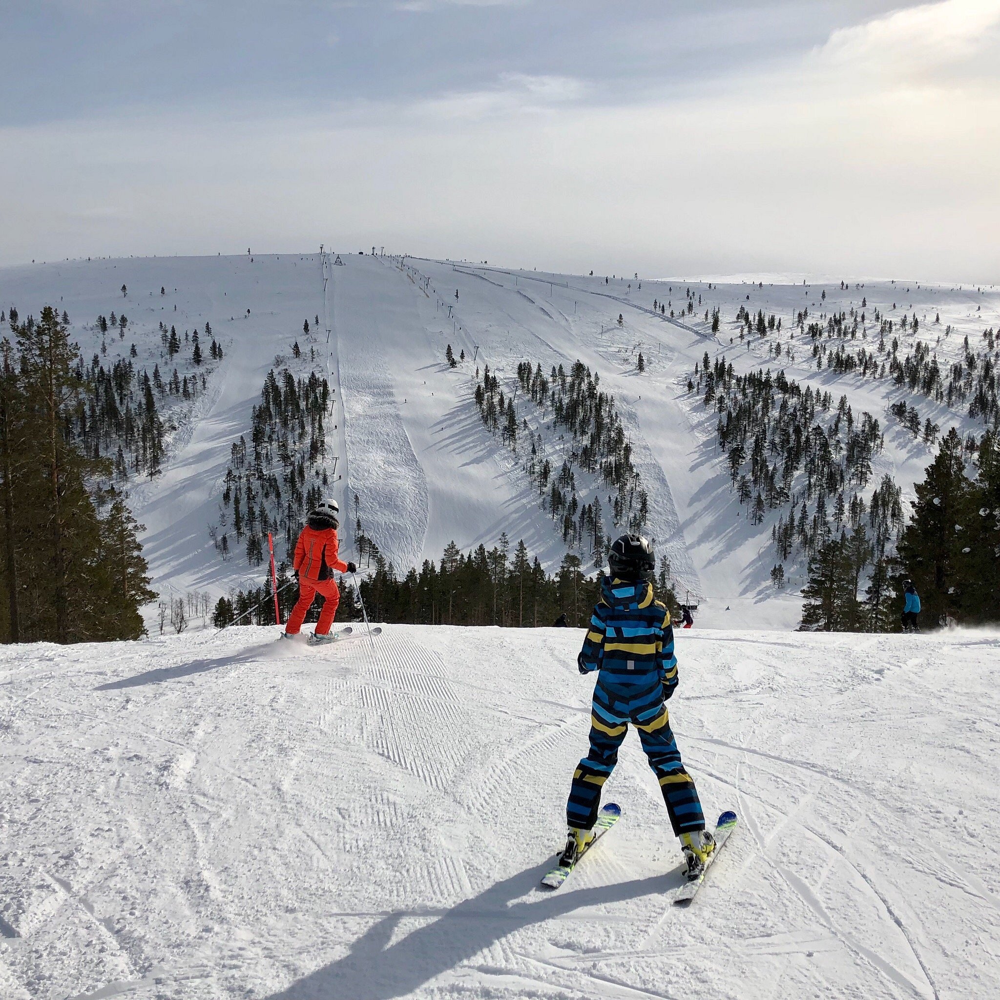 A skier in action amidst a winter sports scene at Saariselkä in Lapland, Finland. The snowy landscape of a ski resort with a ski lift faintly in the background, providing a beautiful Nordic scenery.
