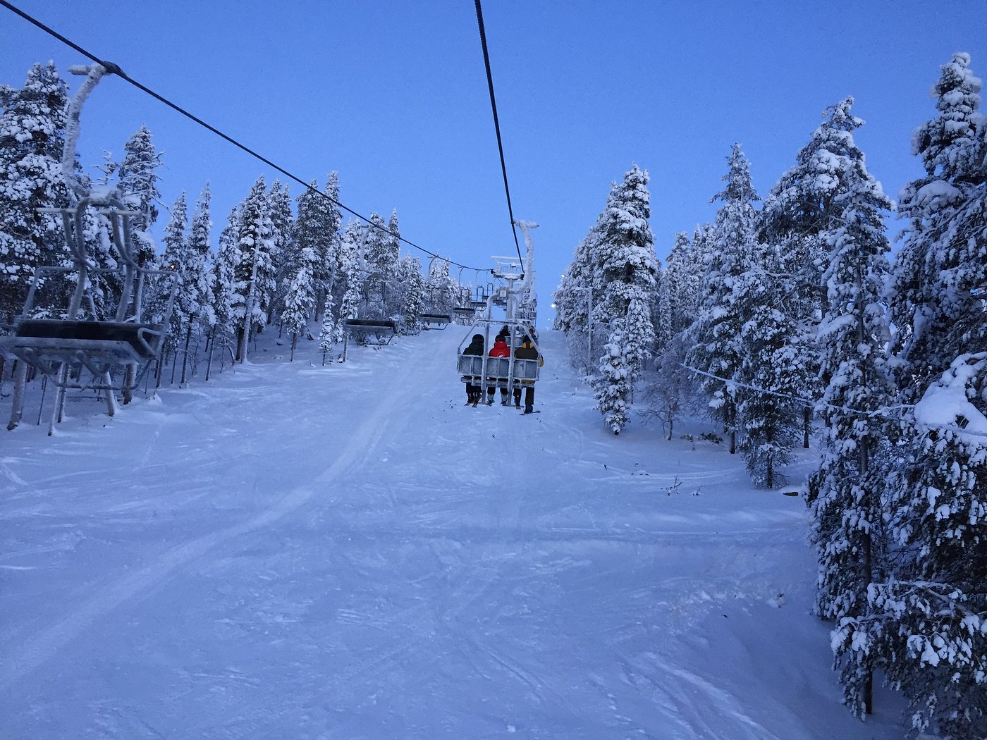 A scenic view of Saariselkä ski resort in Lapland Finland featuring a ski lift snow-covered slopes bustling with skiers with a chalet peeking in the backdrop.