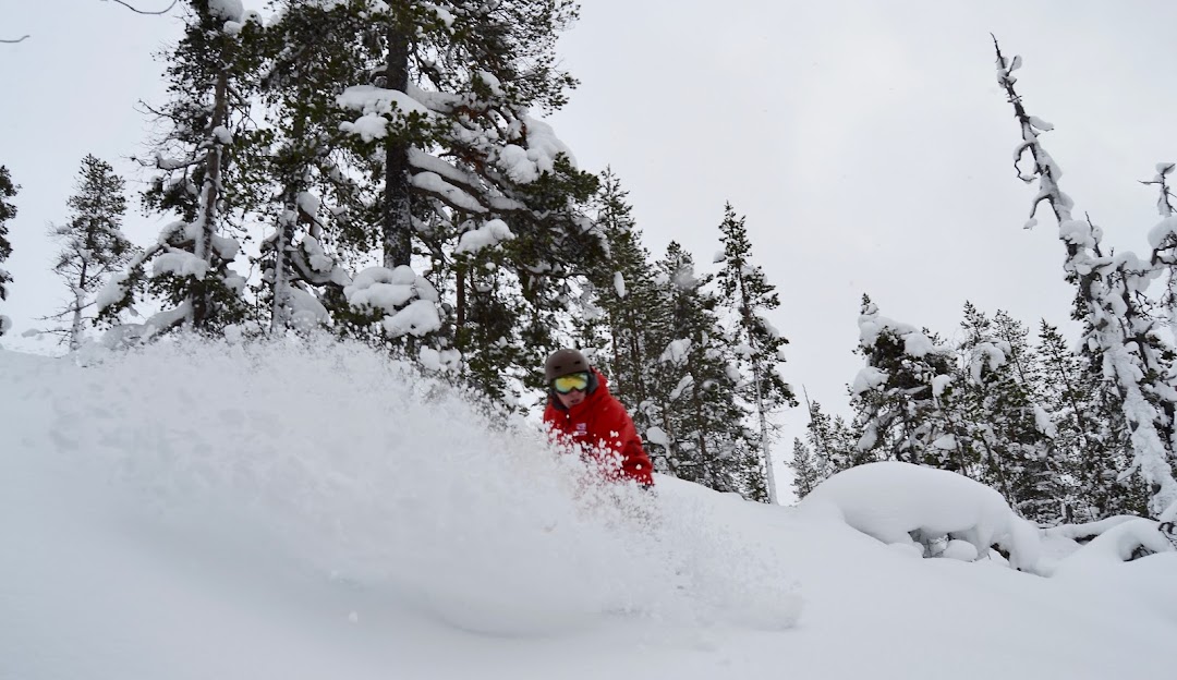 A skier and a snowboarder enjoying winter sports at the Saariselkä ski resort in Lapland, Northern Finland, with a snowmobile nearby in the snow-covered landscape.