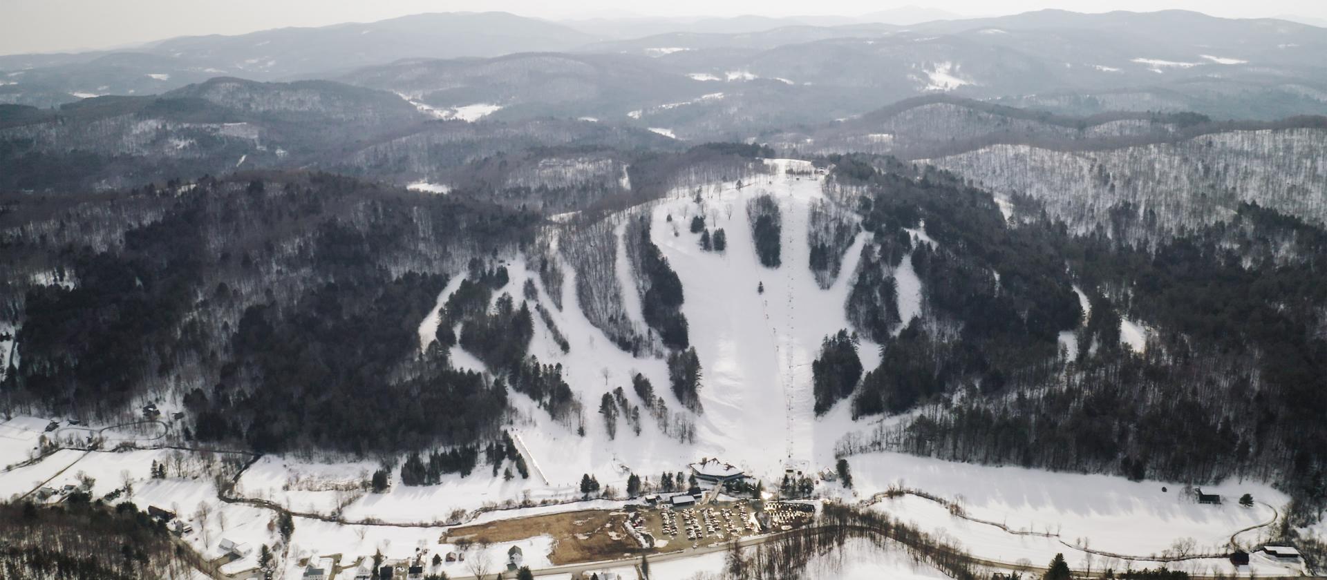 Saskadena Six ski resort in South Pomfret, Vermont, showcasing a winter landscape with snow-covered slopes, a ski lift, and skiers enjoying the winter sports scene.