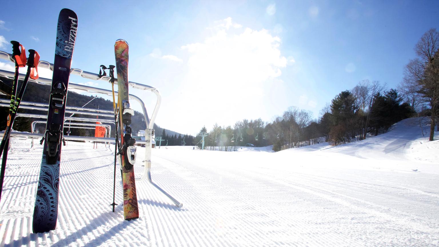 A winter sports scene at Saskadena Six ski resort in South Pomfret, Vermont, featuring a skier, ski lift and various other amenities of the center amidst the snowy landscape.