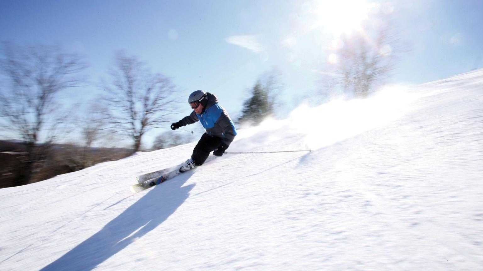 A skier and a snowboarder are enjoying a winter sports scene at Saskadena Six in South Pomfret Vermont. The backdrop features a well-equipped ski resort and a winter sports centre surrounded by snow.