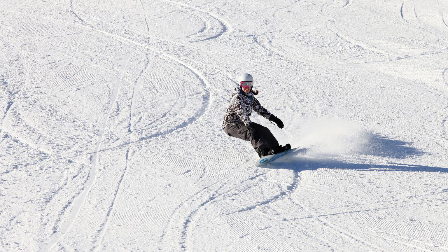A snowboarder caught mid-action at Saskadena Six in South Pomfret, Vermont, showcasing their skills against a backdrop of a pristine, snowy landscape.