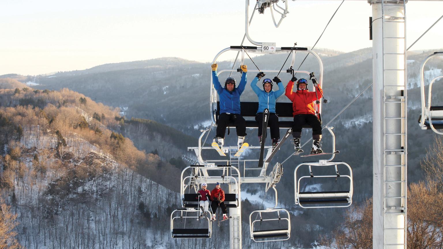 A winter scene at Saskadena Six in South Pomfret Vermont featuring a ski lift in operation families and groups of people enjoying skiing at the resort.