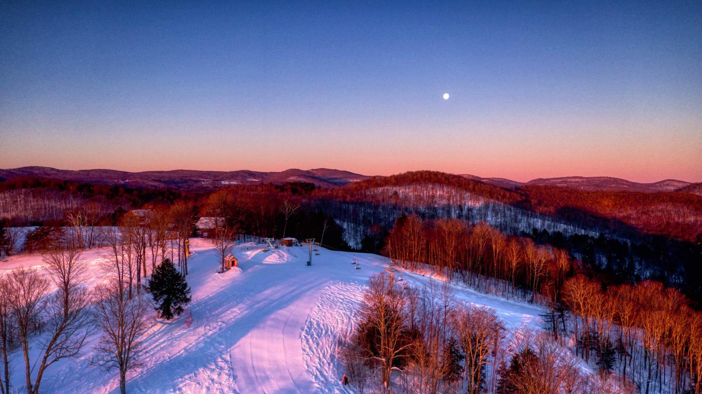 Winter sports scene at Saskadena Six in South Pomfret, Vermont showing a ski resort and a ski lift surrounded by visually stunning winter scenery.