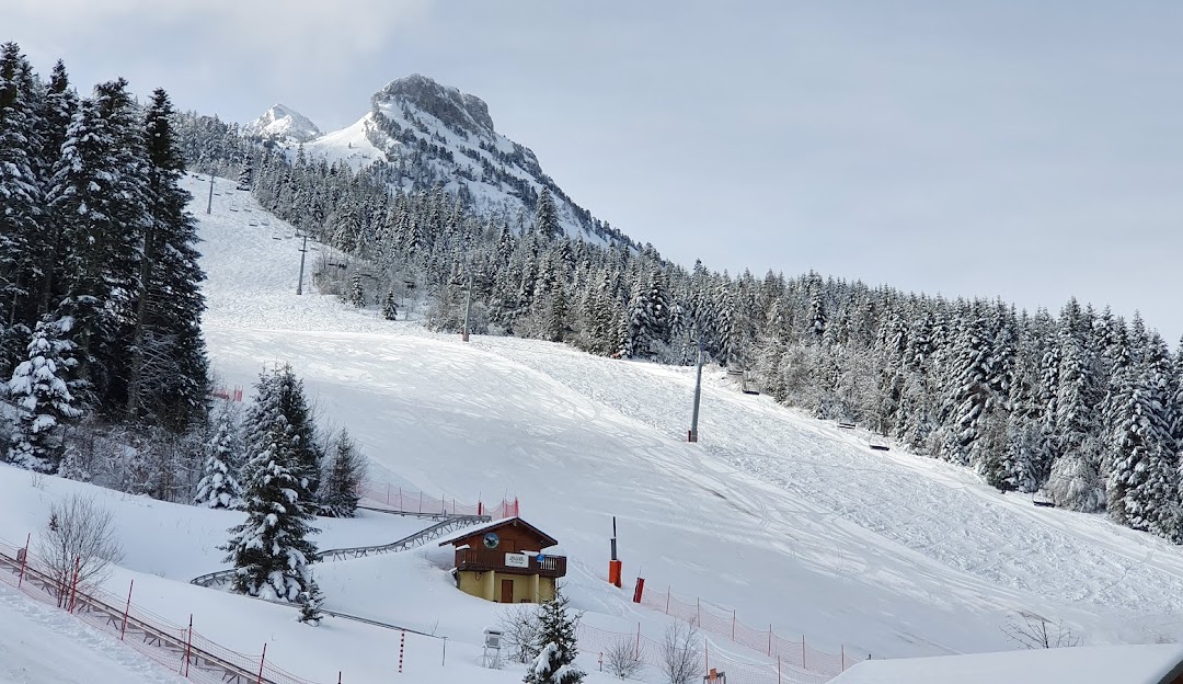 A picturesque view of La Sambuy-Seythenex ski resort in France featuring a ski lift leads to chalets amidst a bustling winter sports center scene.