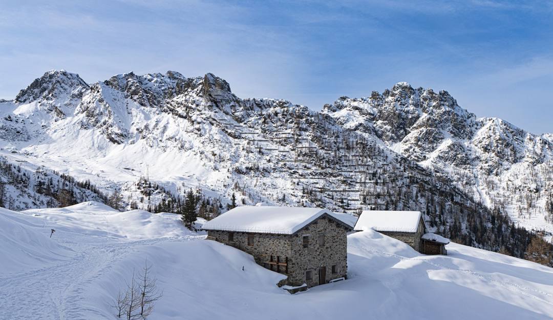 A charming mountain hut and chalet nestled in the snow-covered landscape of Pescegallo Valgerola in Italy, showcasing a stunning winter scenery and a hint of winter sports activity.