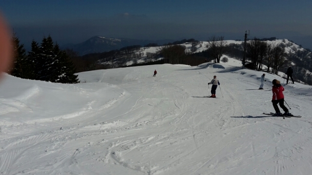 A charming chalet overlooks a winter sports scene at Schia – Monte Caio in Parma Italy. A skier navigates the snowy slopes of the ski resort with a towering mountain visible in the background.