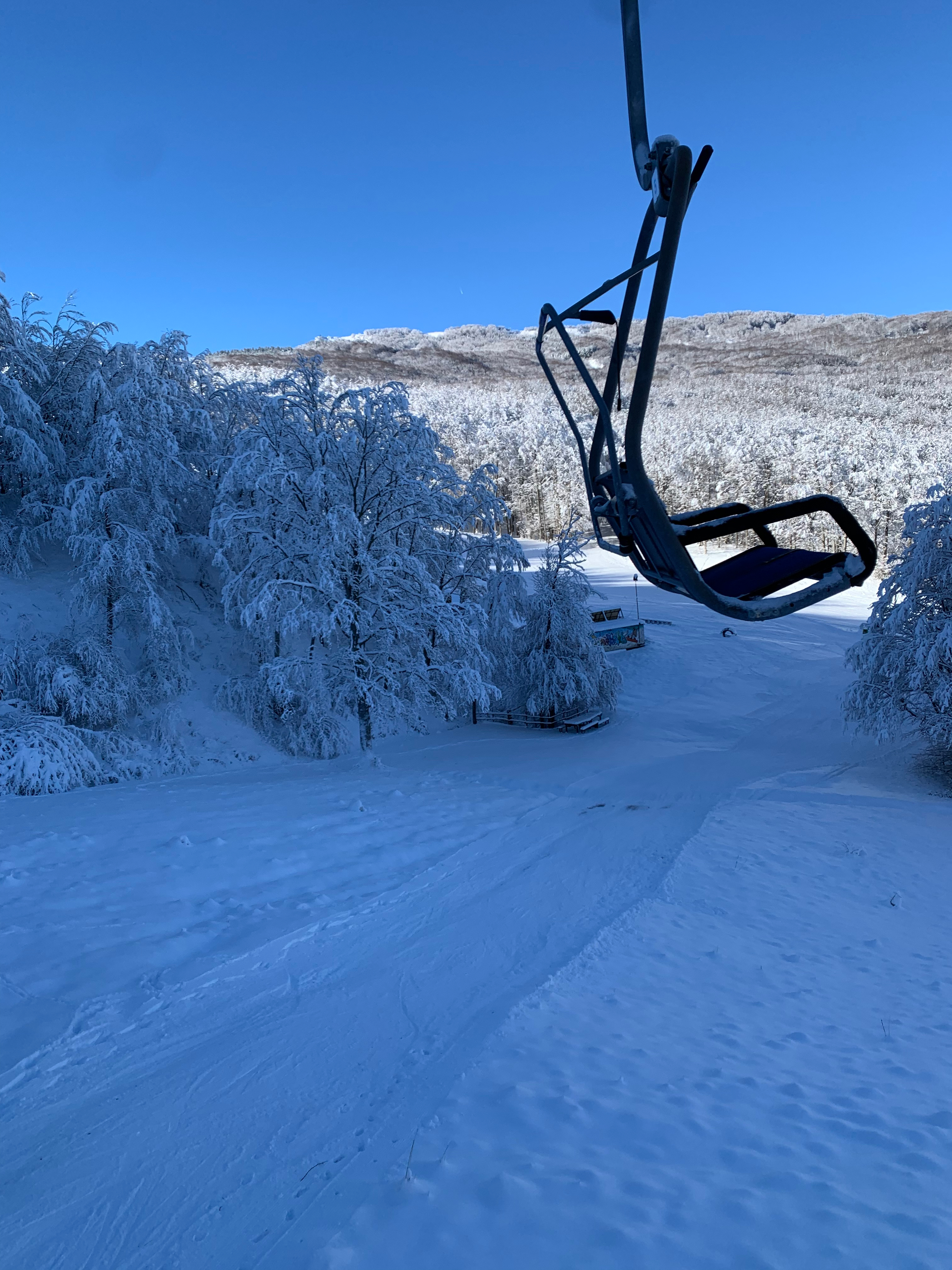 A winter scene at Schia – Monte Caio ski resort in Italy, featuring a ski lift, skiers enjoying the snow-covered slopes, with a snowmobile visible in distance.