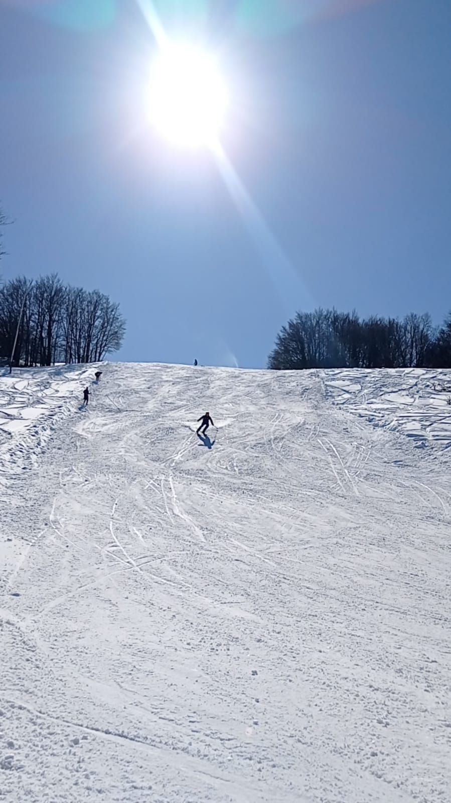 A winter sports scene in Schia – Monte Caio, Parma, Italy featuring a skier, a snowboarder, and a group of people skiing at a ski resort.
