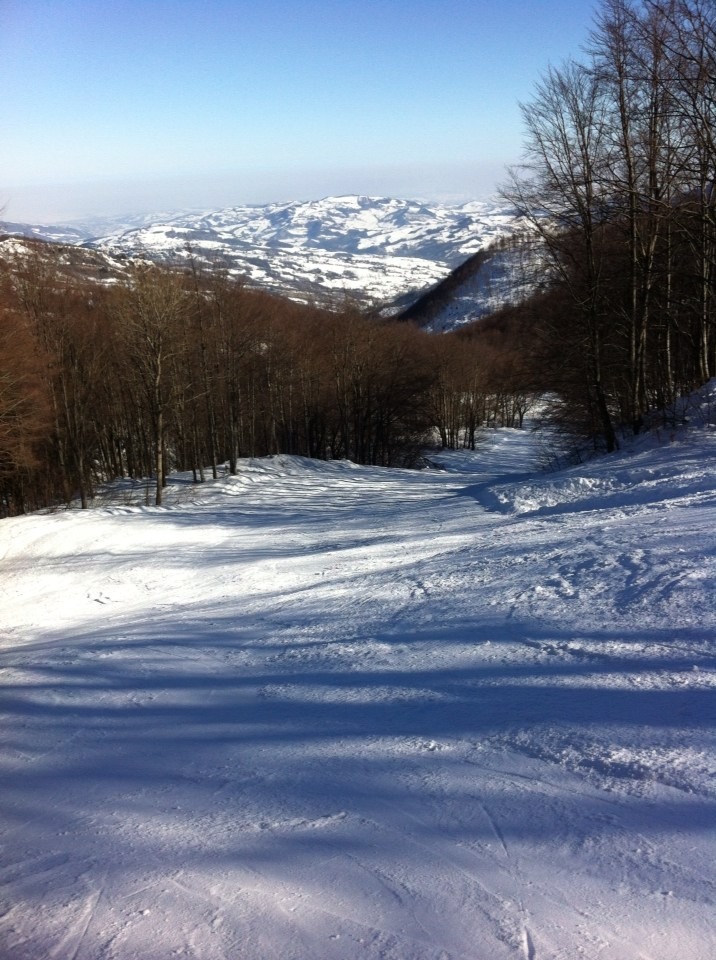 A picturesque view of Schia – Monte Caio in Parma, Italy, featuring a charming chalet nestled amongst the snowy landscape. Skiers and winter sports enthusiasts can be seen enjoying the ski resort.