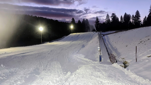 Winter scene at Cloudcroft, New Mexico showcasing a bustling ski resort complete with a lively sports center, a picturesque challet, and a ski lift against a backdrop of snow-covered slopes.