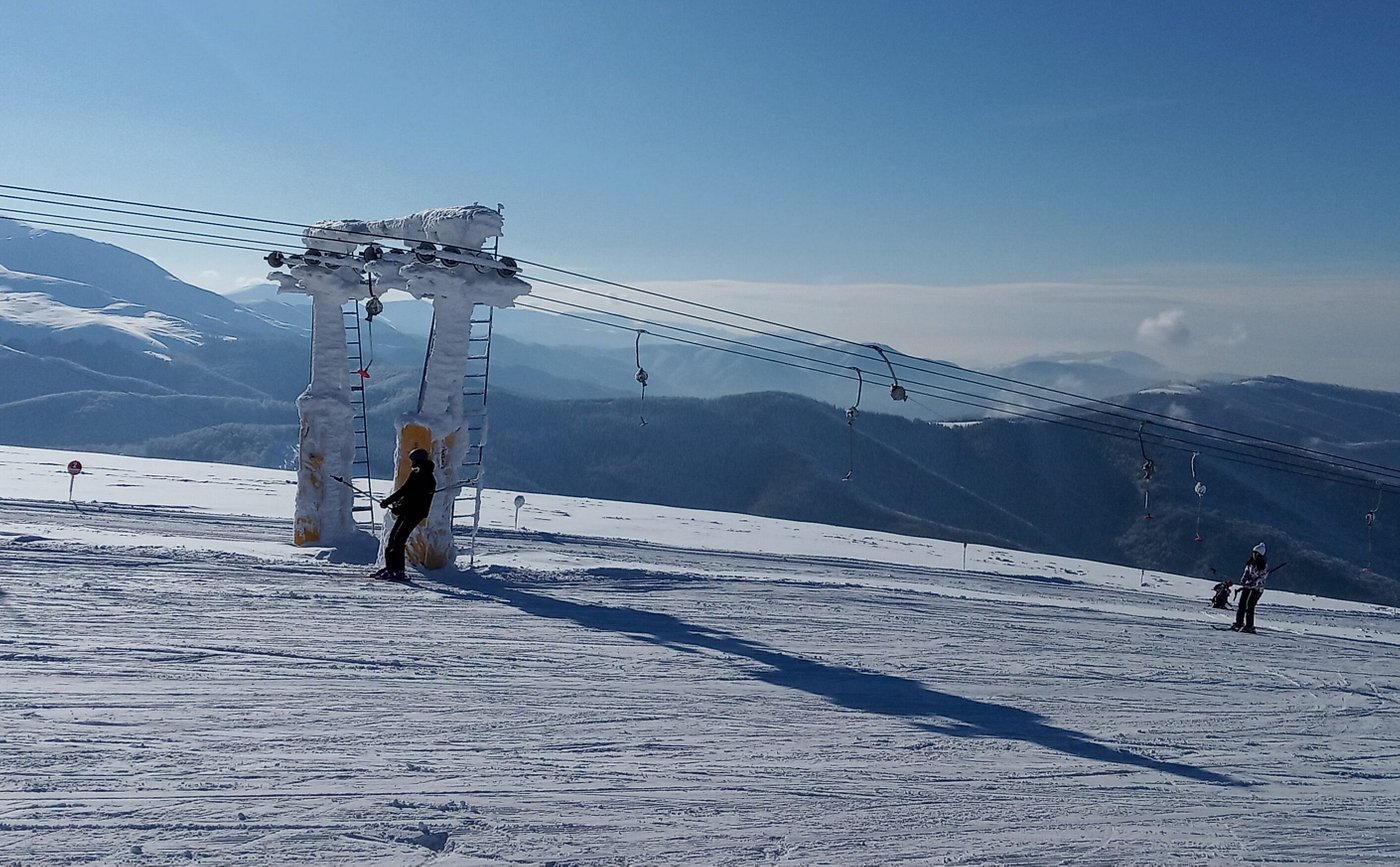A skier gliding down the snowy slopes at Muntele Mic in Romania with a ski lift nearby and a charming challet in the background encapsulating a vibrant winter sports scene at the ski resort.