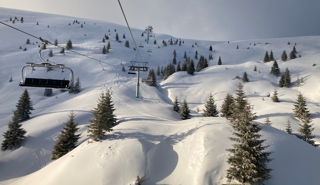 Scenic winter view at Muntele Mic ski resort in Romania featuring a ski lift a cozy chalet and skiers enjoying the snow-covered slopes.