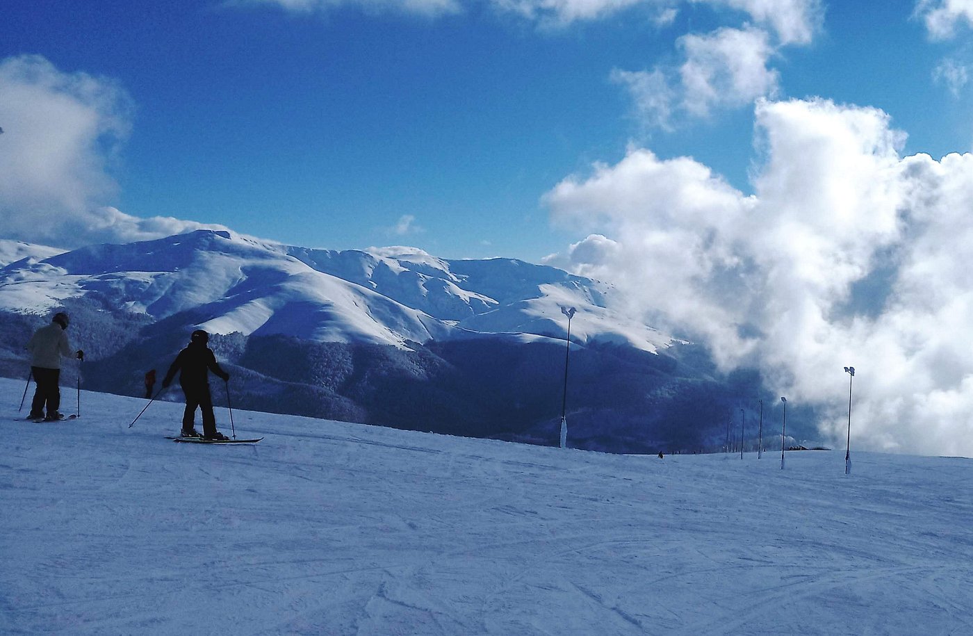 A skier descends a slope at Muntele Mic ski resort in Romania with a charming chalet nestled amongst snow-dusted trees in the background. A ski lift is faintly visible through the winter sports scene.