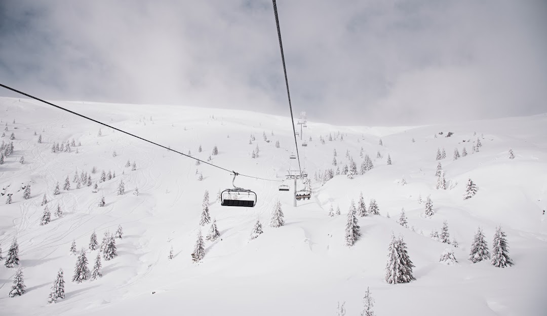 Ski lift ascending Muntele Mic, Romania, against a picturesque winter backdrop, with a skier navigating snow-laden slopes at a ski resort.