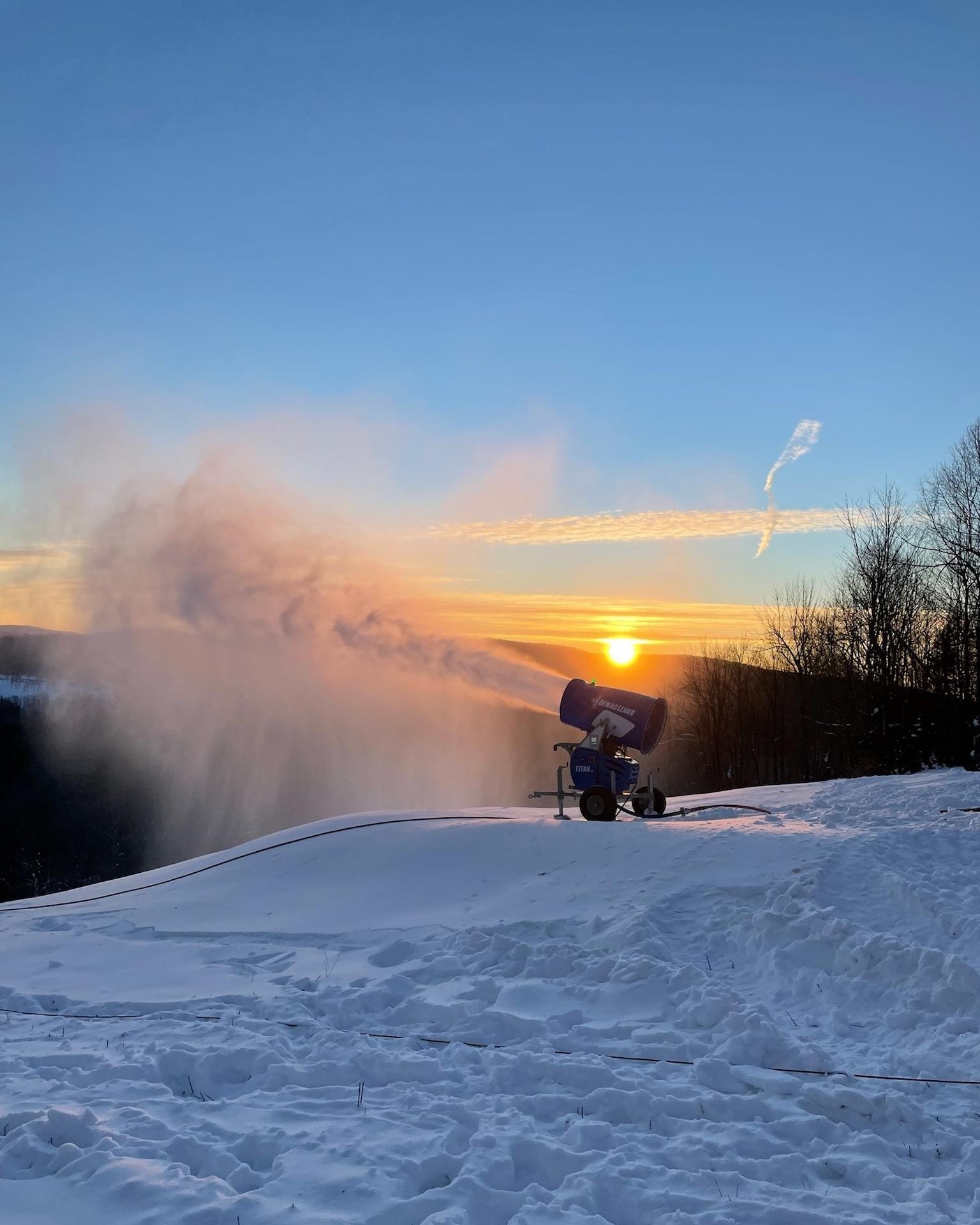 A skier enjoys a winter day at Whaleback ski resort in Enfield New Hampshire. A ski lift and snowmobile can be seen in the background amidst the snowy landscape.