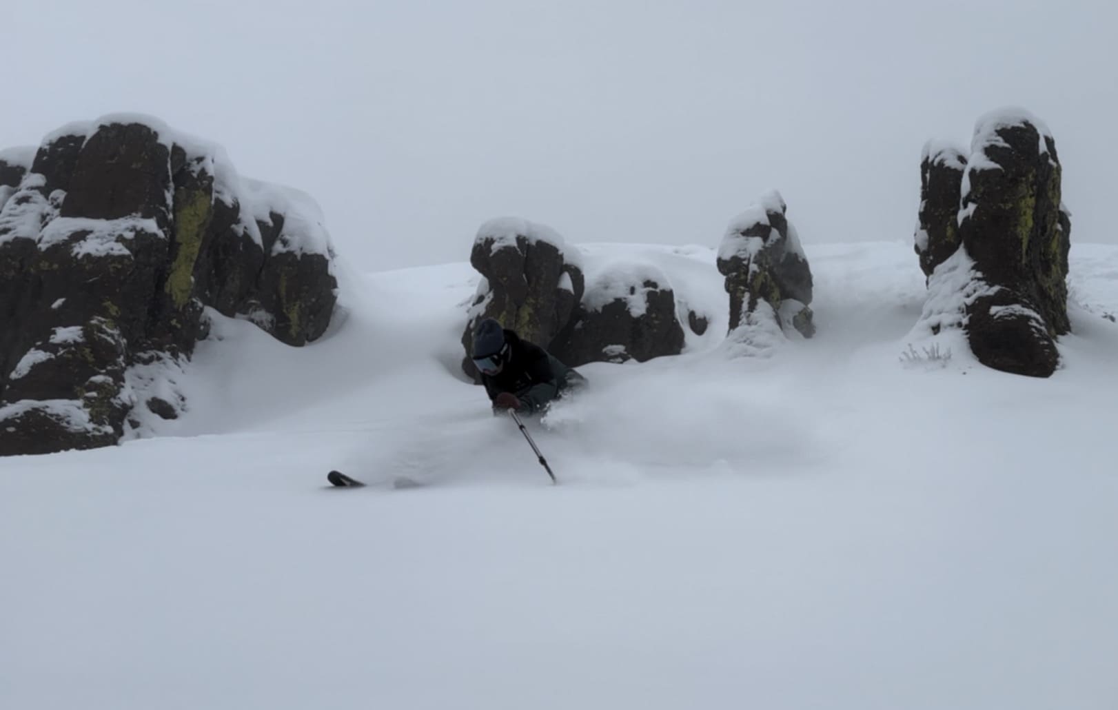 A skier enjoying a run at Magic Mountain Resort in Kimberly, Idaho, with a challet and mountains visible in the snow-covered landscape.