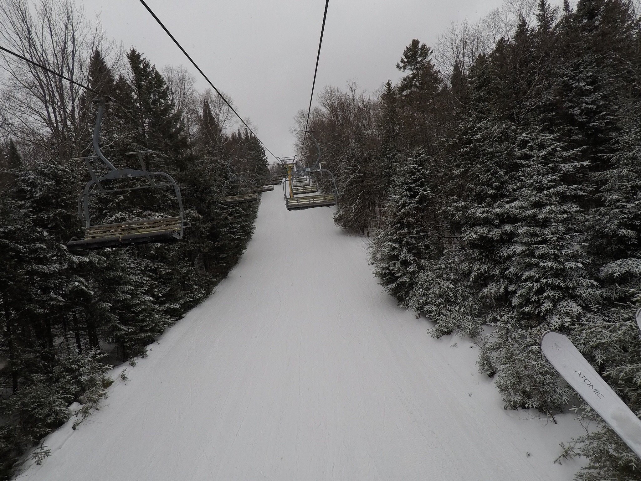 Ski lift ascending at Vallée Bleue, Quebec with winter sports enthusiasts enjoying the snow-covered slopes. A cozy challet and a parked snowmobile can be seen nearby, adding charm to this bustling ski resort.