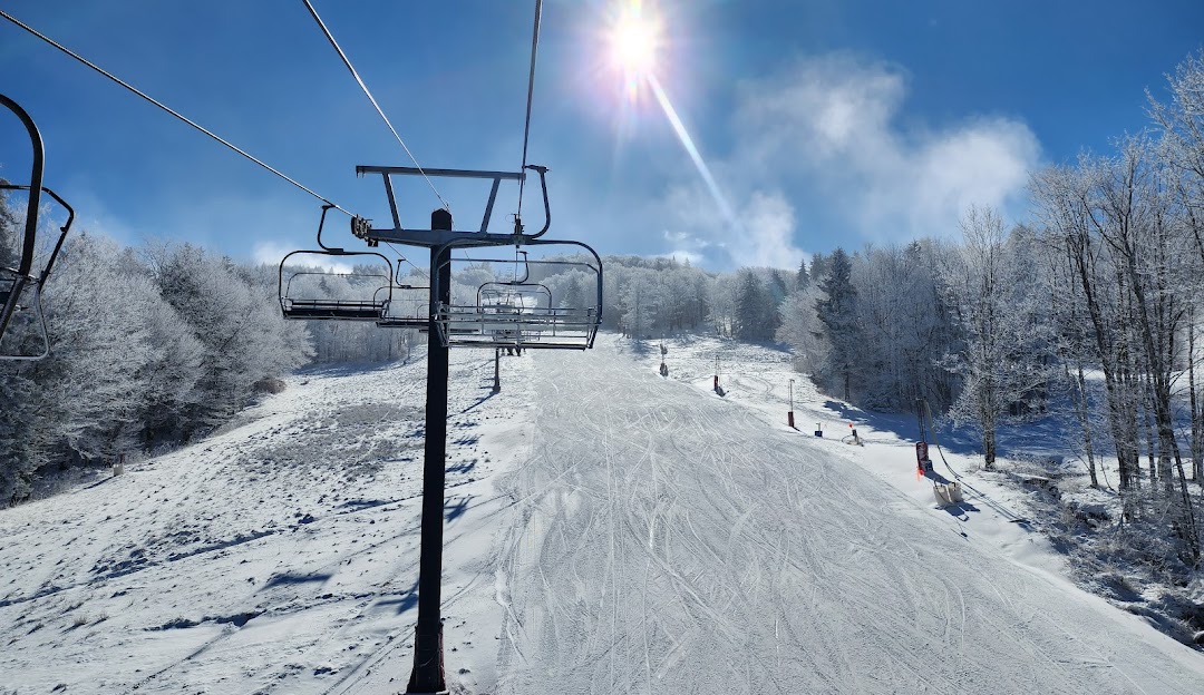 A scenic winter view at Canaan Valley in Davis West Virginia showcasing a bustling ski resort. Skiers glide down the slopes with a ski lift visible in the background and a challet near the base.