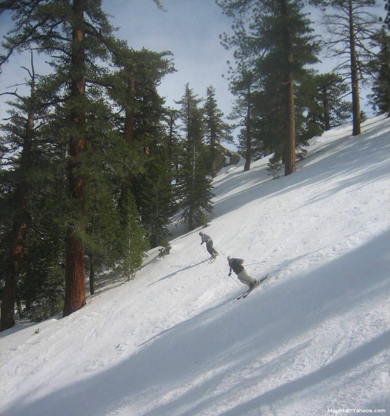 Winter sports scene at Mt Waterman in Pearblossom, California, featuring a skier descending the snowy slope, with a ski lift and a group of people enjoying skiing, possibly a family.