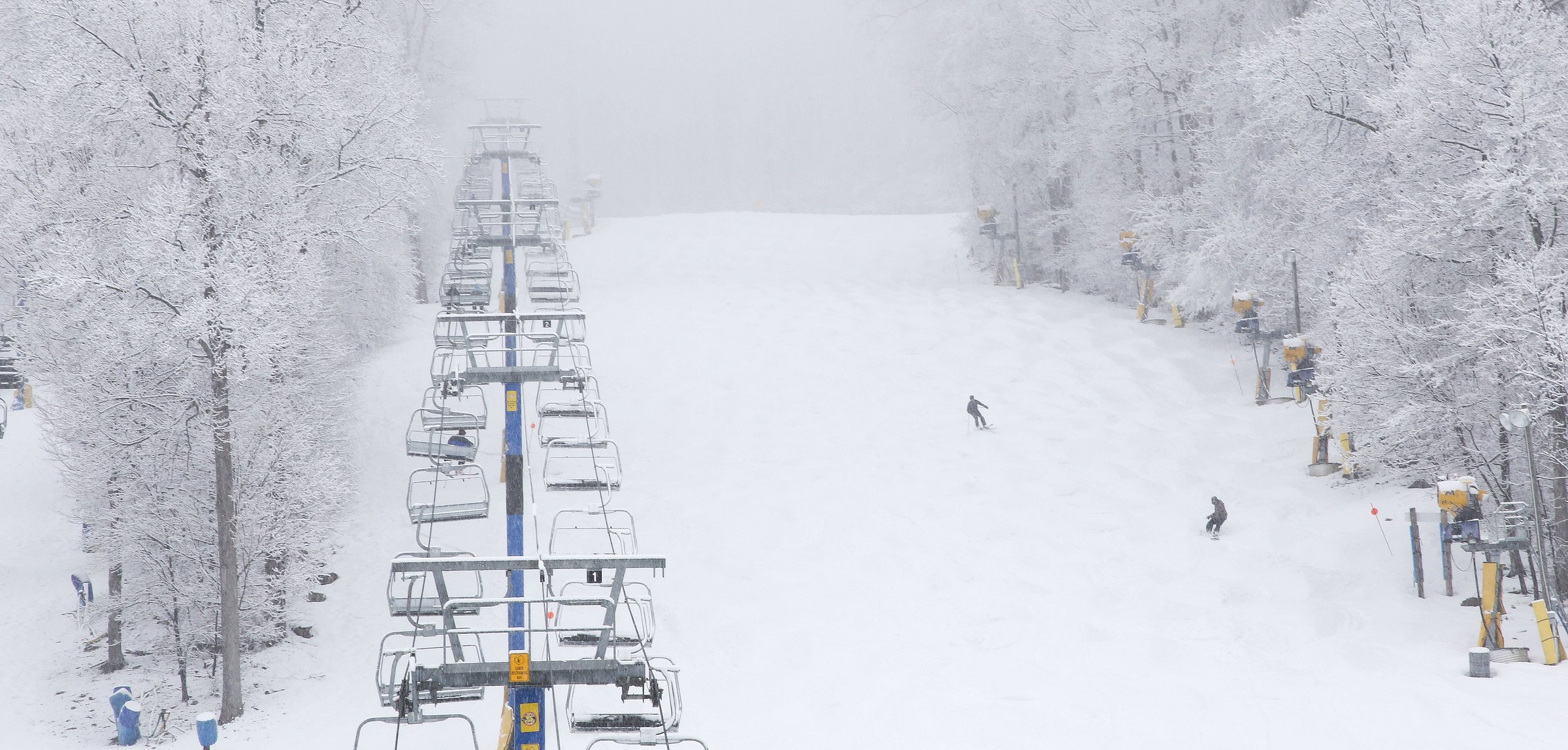 A captivating winter vista at Liberty Mountain Pennsylvania featuring a lively ski resort. Skiers are enjoying the slopes with a ski lift conveniently transporting them to the mountain top. The scene is enveloped by a stunning winter landscape.