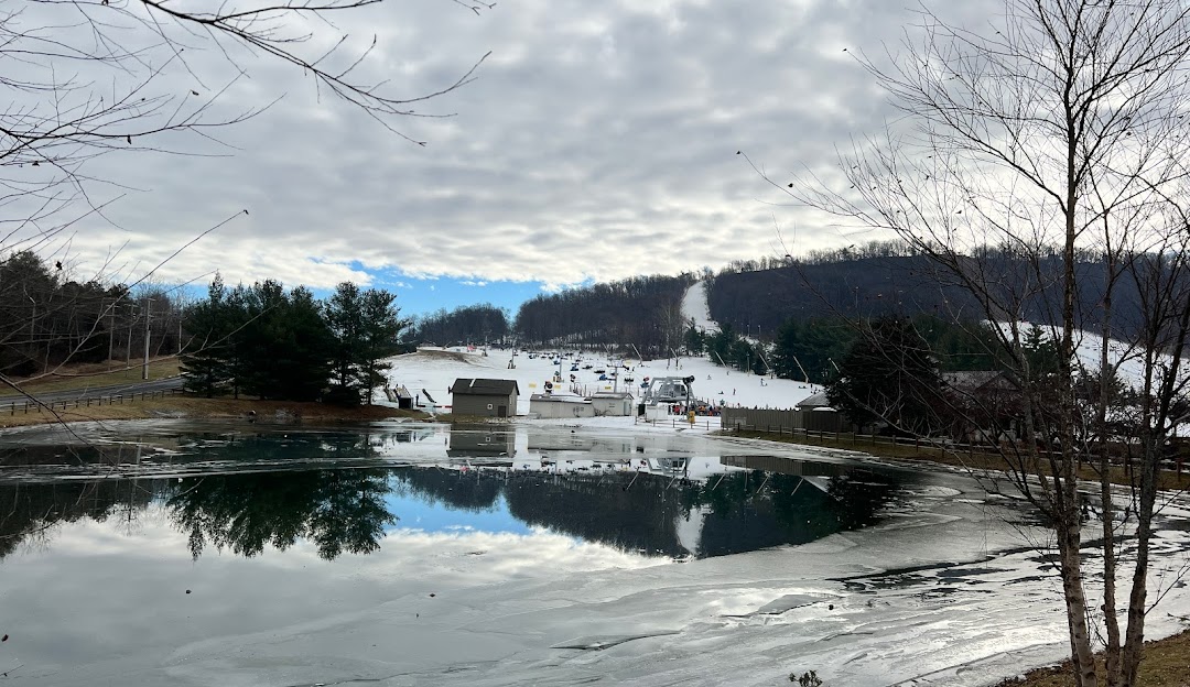 A winter sports scene at Liberty Mountain in Fairfield Pennsylvania featuring a chalet beside a lake amidst a stunning winter landscape.