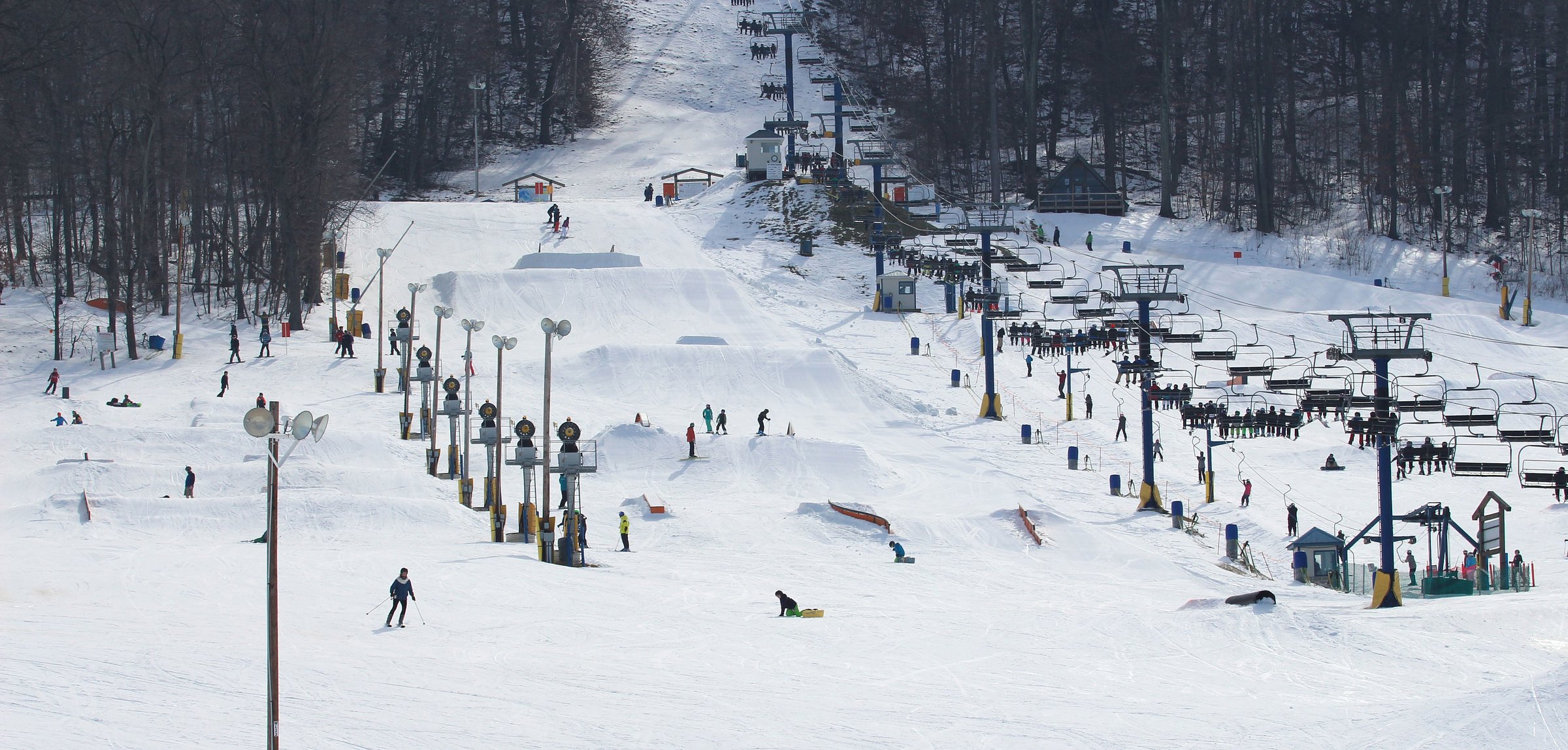 Winter scene at Liberty Mountain in Fairfield, Pennsylvania, a popular ski resort. Skiers traverse snowy slopes, some using the lift for ascent. The stunning winter landscape completes the picturesque view.